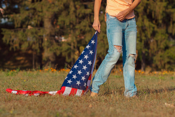 Woman with a flag of United States of America in the hand, outdoors, soft focus background - Photo, Image