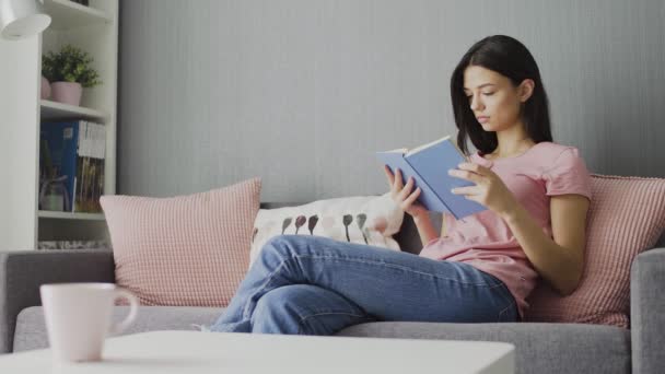 Vrouw die een boek leest en thuis op de bank zit te realxen - Video