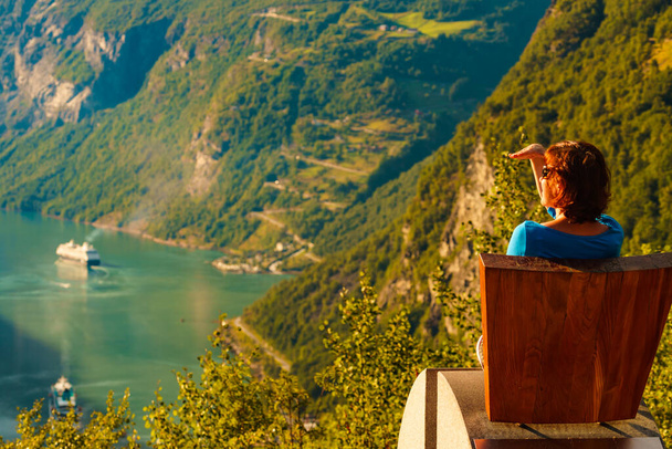 Tourism vacation and travel. Female tourist enjoying view over Geirangerfjord from Flydalsjuvet viewpoint seat, Norway. Tourist attraction. - Фото, зображення