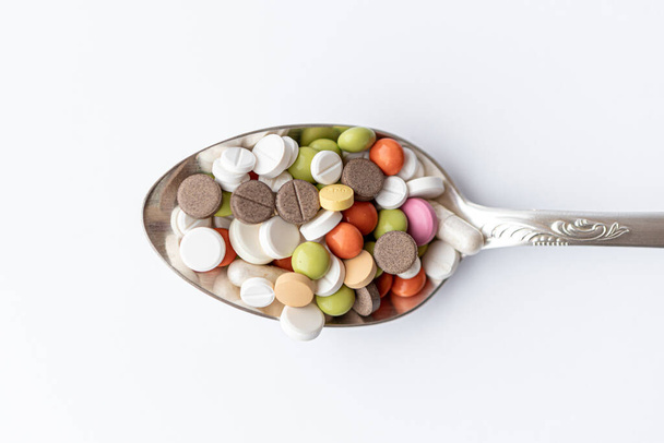 Medicine and health, treatment, pharmaceutics, coronavirus, pandemic, epidemic concept - layout one silver big tablespoon with multi-colored tablets and capsules on a white background copy space. - Fotografie, Obrázek