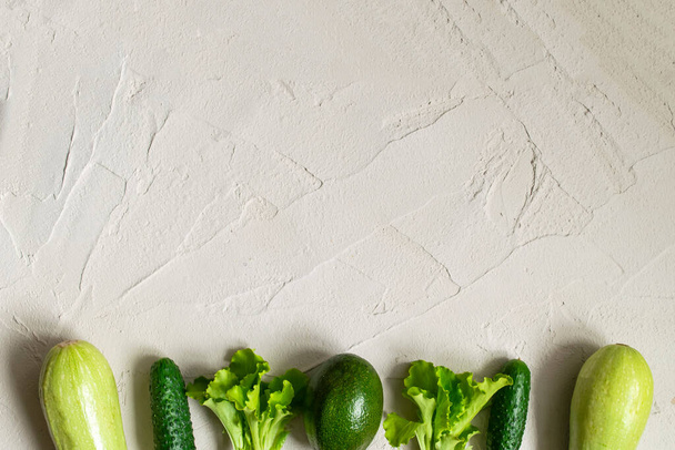 Assortment of fresh green organic vegetables. zucchini, cucumber, onion, avocado, lettuce, on a concrete background. flat lay copy spase - Fotó, kép