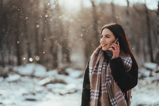 女が携帯電話で話してる。寒い冬の日に携帯電話で話している笑顔の女の子. - 写真・画像
