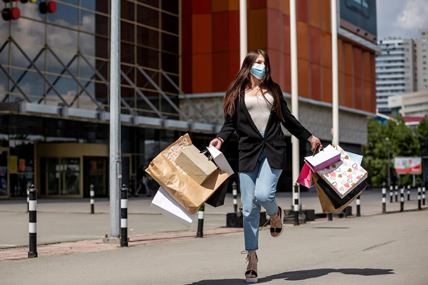 girl in medical mask dances with purchases near the shopping center - Photo, Image