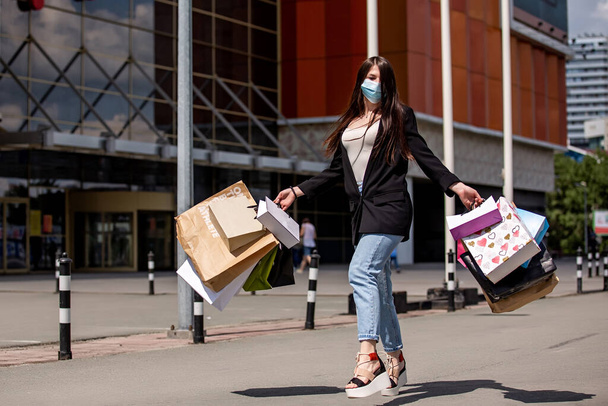 girl in medical mask dances with purchases near the shopping center - Фото, зображення