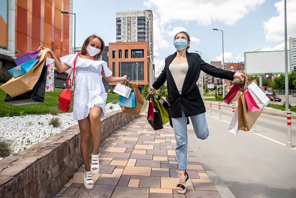 girl in medical mask dances with purchases near the shopping center - Foto, Imagen