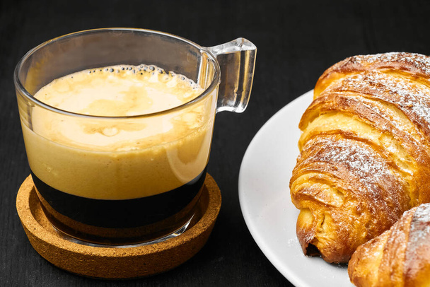 Kopje koffie en vers gebakken croissants op een donkere tafel. Geserveerd ontbijt concept. Frans gebak van bladerdeeg  - Foto, afbeelding
