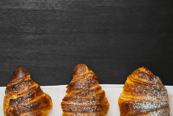 Vlakke lay van drie croissants op een zwarte achtergrond met kopieerruimte.  - Foto, afbeelding