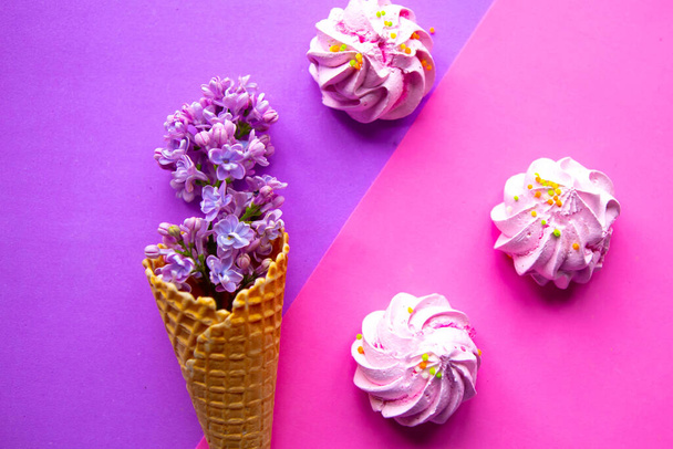 Lilac blooming branch in waffle cone and meringue on geometric purple background.  - Photo, Image