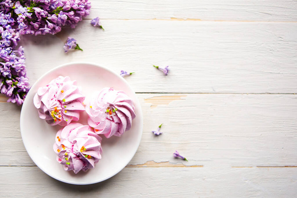 Tasty meringue and lilac blooming branch on wooden table. Flat lay, top view, copy space for the text - Fotografie, Obrázek