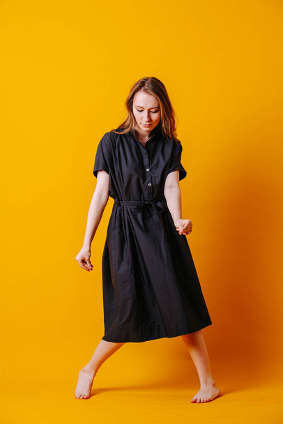 Spirited young woman in black dress doing crazy cool dance over orange - 写真・画像