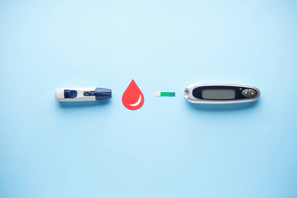 Concepto de diabetes plano laico. Glucosímetro digital y lápiz lanceta sobre fondo azul. Medidor de glucosa en sangre
. - Foto, Imagen