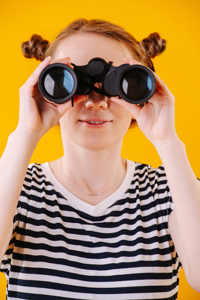 Cute ginger woman in a striped dress looking in binoculars. Close up. - Foto, Imagem