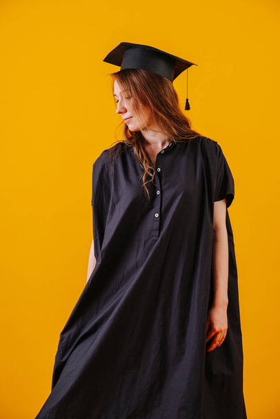 Woman in graduation gown and hat over orange background. - Fotografie, Obrázek