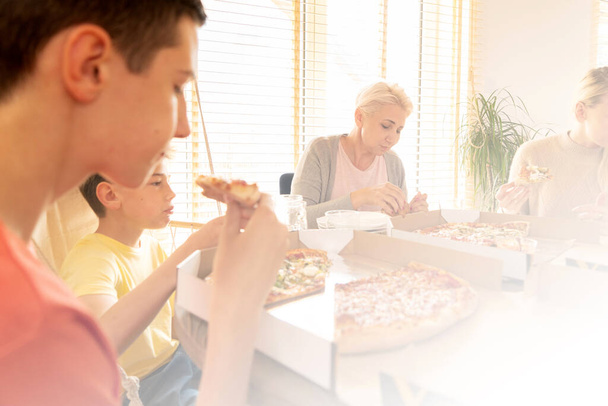 La familia pasa un buen rato juntos en casa. Mamá con niños divirtiéndose, comiendo pizza. Confort hogar
. - Foto, imagen