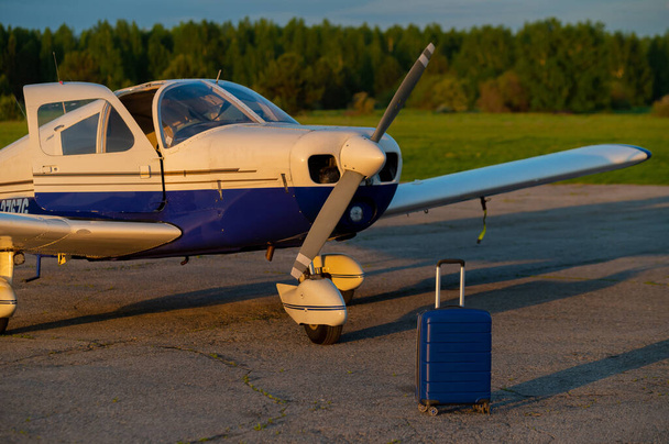青いスーツケースと着陸した小さなプライベートジェット。4人乗りの飛行機は、空気タクシー用プロペラ付き。自己旅行の概念。VIPのための飛行機. - 写真・画像