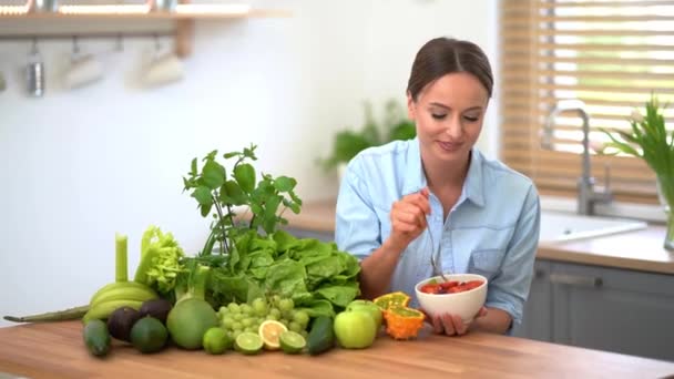 Glückliche Frau isst Salat, während sie in ihrer Küche sitzt - Filmmaterial, Video