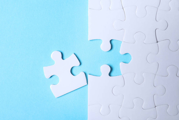 Blank white puzzle with separated piece on light blue background, flat lay - Fotó, kép