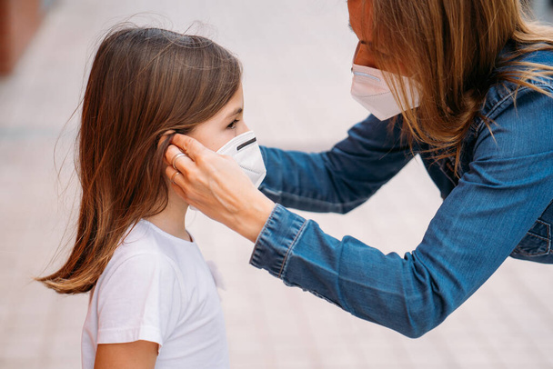 Mother putting face mask on her little daughter on the street - Valokuva, kuva