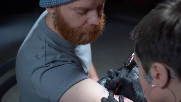 Un hombre barbudo ve a un tatuador llenar un tatuaje
 - Foto, imagen