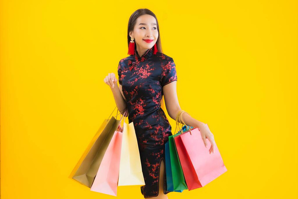 Portrait belle jeune femme asiatique porter robe chinoise avec sac à provisions, téléphone portable intelligent, carte de crédit pour le Nouvel An chinois sur fond jaune isolé
 - Photo, image