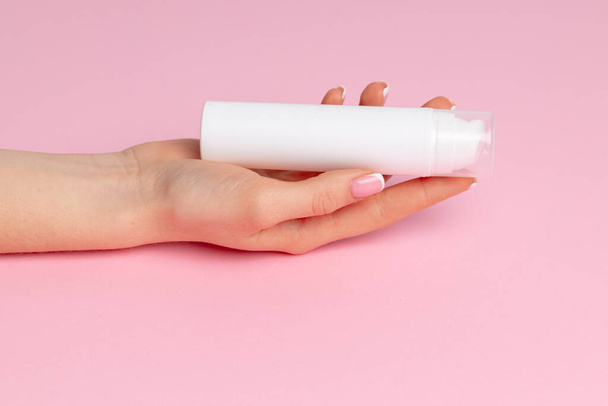 Female hand holding skincare product bottle on pink - Foto, afbeelding