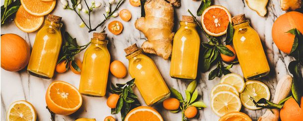 Immune boosting vitamin health defending drink. Flat-lay of fresh turmeric, ginger, citrus juice shot in bottles over marble background, top view, wide composition. Vegan Immunity system booster - Valokuva, kuva