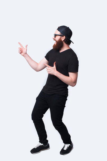 Teljes hosszúságú fotó egy elképedt szakállas hipszter férfiról, aki elfelé mutat. - Fotó, kép