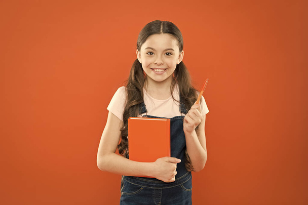Doing research. literature lesson. back to school. happy little girl with notebook. school girl read book on orange background. writing notes. kid diary. poetry and novel. modern education - Foto, Imagen