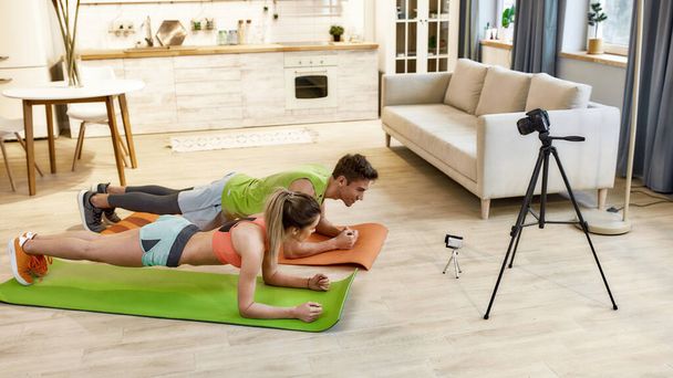 Shooting workout. Young couple recording video blog or vlog about healthy lifestyle on camera while exercising at home. Fitness, workout and vlogging concept - Фото, изображение