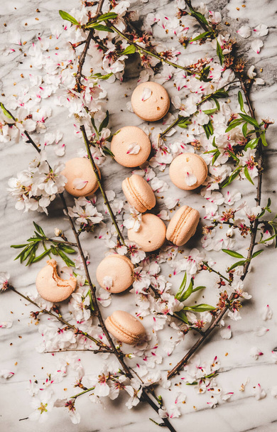 Food texture, wallpaper and background. Flat-lay of sweet macaron cookies and white spring blossom flowers and branches over white marble background, top view, vertical composition - Foto, imagen