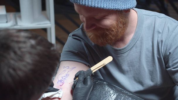 Ο δάσκαλος του τατουάζ βάζει ένα τατουάζ σε έναν άντρα. Συρόμενη - Φωτογραφία, εικόνα