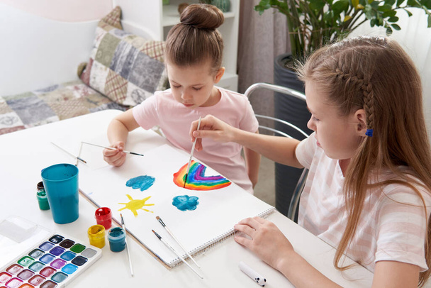 Twee gelukkige zusters schilderen thuis, regenboog tekening - Foto, afbeelding