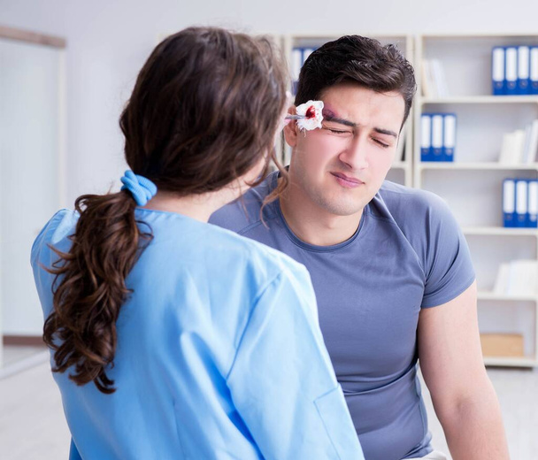 Hombre joven visitando a traumatóloga femenina con ojo morado - Foto, imagen