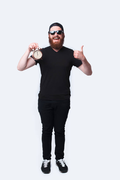 Full length photo man with beard wearing sunglasses and holding alarm clock - Photo, Image