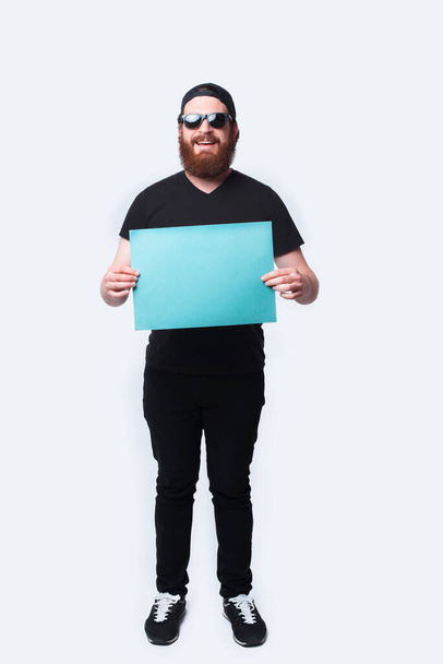 Foto de cuerpo entero hombre barbudo feliz sosteniendo papel en blanco azul sobre blanco
 - Foto, imagen