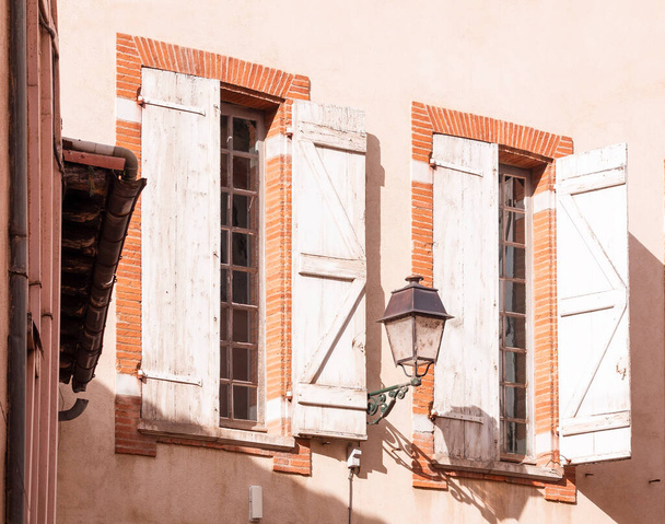 Παράθυρα με παντζούρια και ένα φανάρι στον τοίχο ενός παλιού σπιτιού σε μια ηλιόλουστη μέρα - Φωτογραφία, εικόνα
