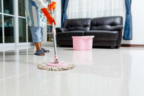Evdeki yerleri temizlerken ıslak bez kullanan koruyucu eldivenli Asyalı güzel bir genç kadın evi temizlemek için paspas kullanıyor.. - Fotoğraf, Görsel