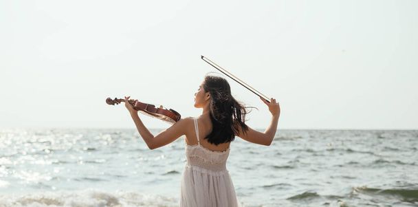 Girl playing violin on the sea. - Фото, изображение