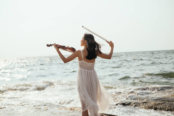 Дівчина стоїть на морській скелі і грає на скрипці
. - Фото, зображення