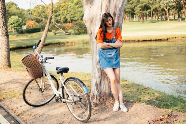 Linda chica apoyada en un árbol cerca de la bicicleta
. - Foto, imagen
