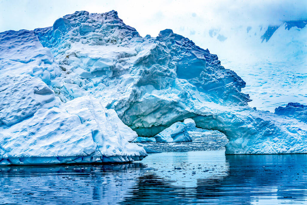 スノーフローティングブルー氷山アーチ反射パラダイスベイスキントープコーブ南極。氷河の氷の青のため、空気の雪の外に圧迫. - 写真・画像