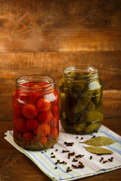 Jars of pickled homemade pickled cherry tomatoes gherkins on a wooden table. Vertical photo - Photo, Image