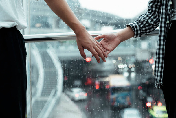 Nahaufnahme der Hände des Paares, die sich fest mit einem Regen auf einem Glas als Hintergrund halten. - Foto, Bild