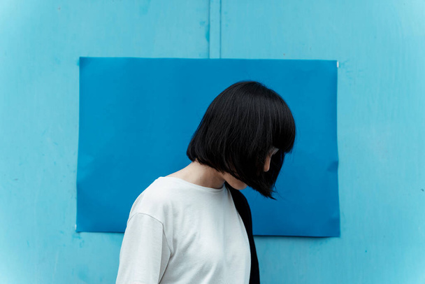 短い髪の女性彼女の顔を隠すとき、彼女は光と濃い青の前に立って. - 写真・画像