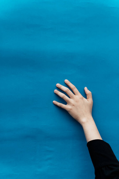 De hand van een vrouw verheft zich op de blauwe achtergrond om iets te vangen.. - Foto, afbeelding