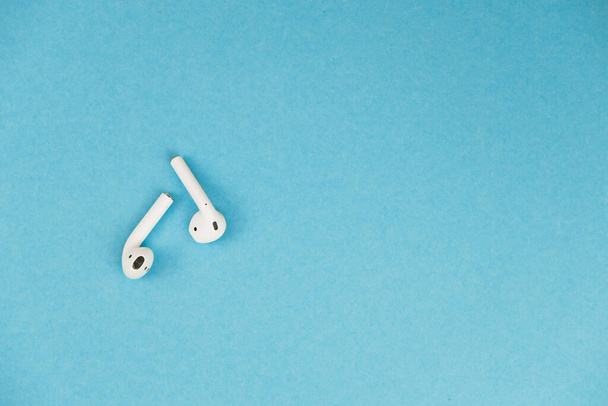 Wireless white headphones on blue background. Place for a text. - Foto, afbeelding