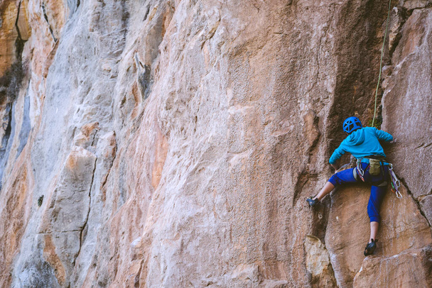 Una donna in casco si arrampica su una bellissima roccia arancione. Attrezzatura protettiva per arrampicata. Sicurezza nell'arrampicata. L'arrampicatore supera una via difficile su un terreno naturale. Arrampicata in Turchia. - Foto, immagini