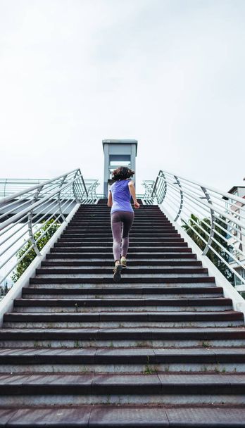 A woman runs up the stairs. Running training in the city. Jogging. Reaching the goal. The desire for victory. Aspiration. Workout. - Zdjęcie, obraz