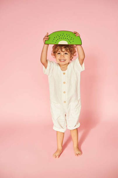 Smiling red-haired boy with decorative watermelon on pink background. - Fotó, kép