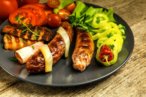 Grilled sausages with bacon and cheese on a black plate. Vegetables for meat. Home preparation for a party. - Foto, Bild